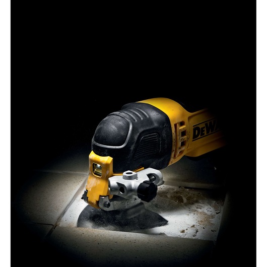 A DEWALT oscillating multi-tool cutting through ceramic tiles, shown in close-up with debris and dust around the cutting area.