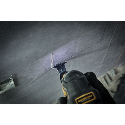 A close-up of a DEWALT oscillating tool being used to cut a marked rectangular shape into a drywall surface.
