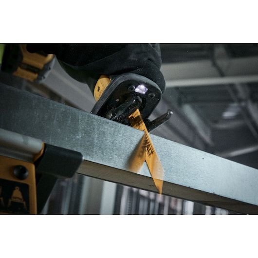 Close-up of a DEWALT reciprocating saw cutting through a metal beam, with the yellow saw blade visible and illuminated by an LED light.