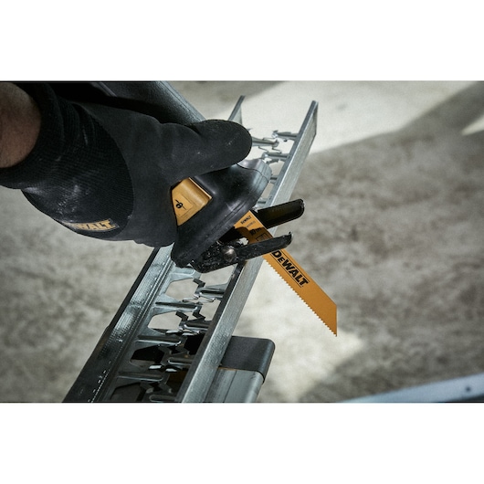 Close-up of a DEWALT saw blade cutting through a metal piece. The person operating the tool is wearing a black DEWALT glove.