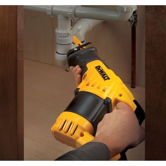 Person using a DEWALT reciprocating saw to cut pipes under a sink in a cabinet.