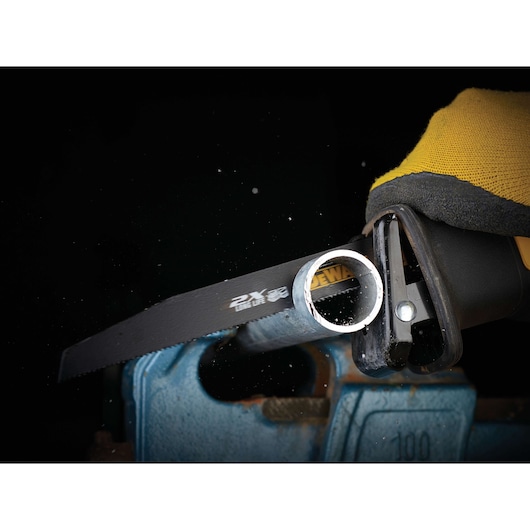 DEWALT saw blade cutting through a metal pipe held in a vise, with a gloved hand operating the tool.