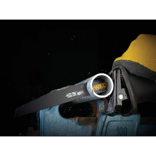 Close-up of a DEWALT saw blade cutting through a metal pipe using a power tool, glove visible.