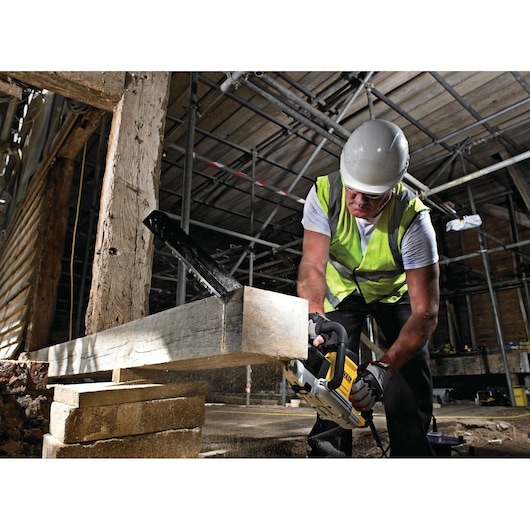Worker uses DEWALT saw to cut wood beam at a construction site, wearing safety gear and a hi-vis vest.