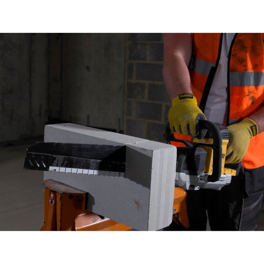Person using a DEWALT saw with gloves to cut a concrete block indoors.