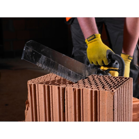 Person using DEWALT tool to cut a large, hollow brick. Tool has yellow handle and gloves are worn.