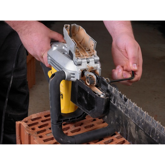 Person uses a hex key to adjust or maintain a DEWALT saw on a brick surface.