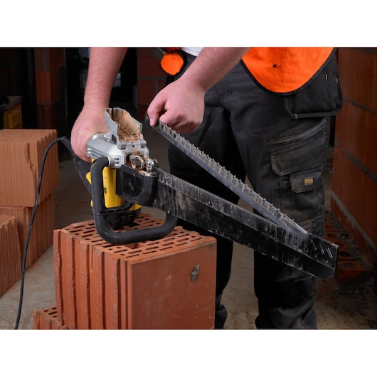 Person holds a DEWALT power tool with a long blade, used for cutting bricks at a construction site.