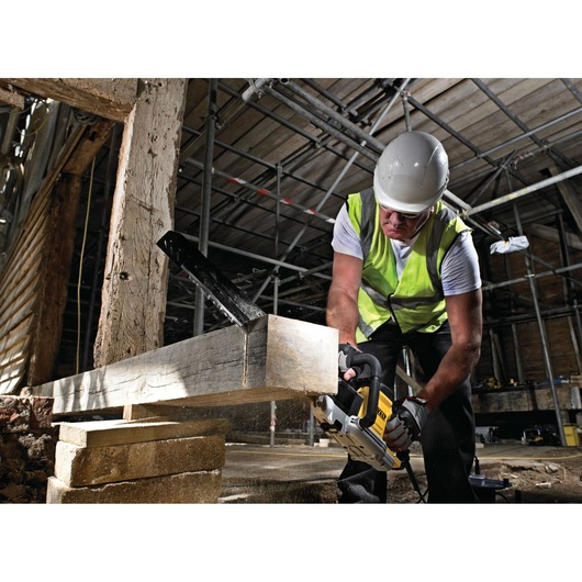 A construction worker wearing a safety helmet and high-visibility vest is using a DEWALT power tool to cut a wooden beam at a worksite. The background shows scaffolding and timber structures.
