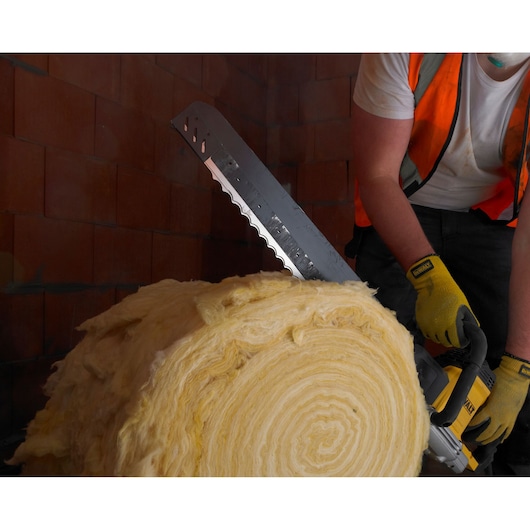 Person cuts insulation roll with a DEWALT saw, wearing gloves and safety vest in a brick-walled area.