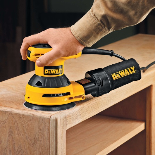 A person using a DEWALT electric sander to smooth the edge of a wooden furniture piece.