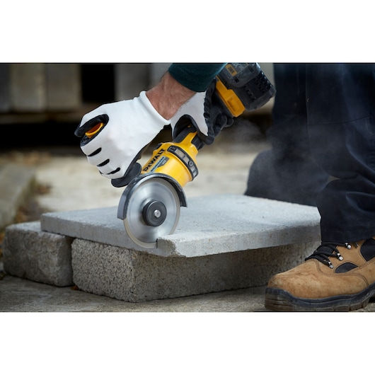 Person cuts concrete block with a DEWALT power tool, wearing gloves and work boots outdoors.