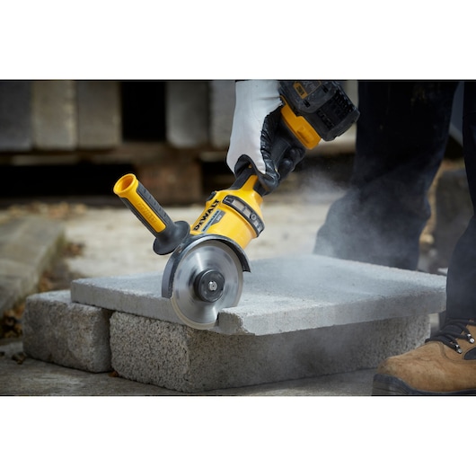 DEWALT DT3712 tool cutting concrete block outdoors, with dust and worker's gloved hand visible.