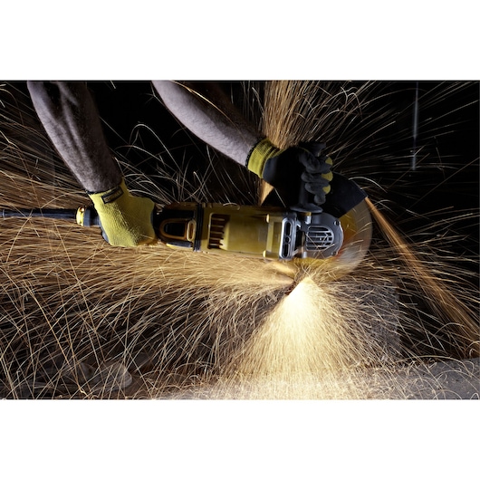 A person uses a DEWALT angle grinder, producing bright sparks while cutting material, wearing protective gloves.