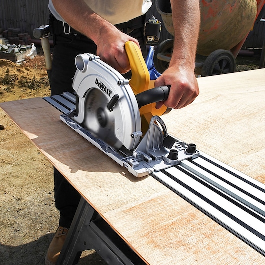 A person uses a DEWALT circular saw with a guide rail to cut a sheet of plywood outdoors.