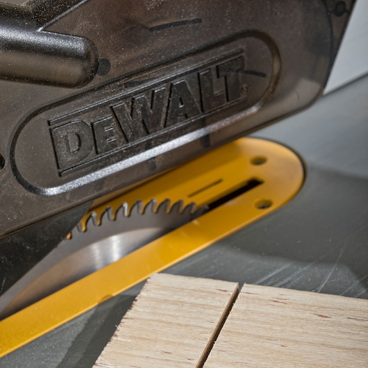 Close-up of a DEWALT circular saw blade cutting through a piece of wood. The DEWALT branding is visible on the saw's protective cover.