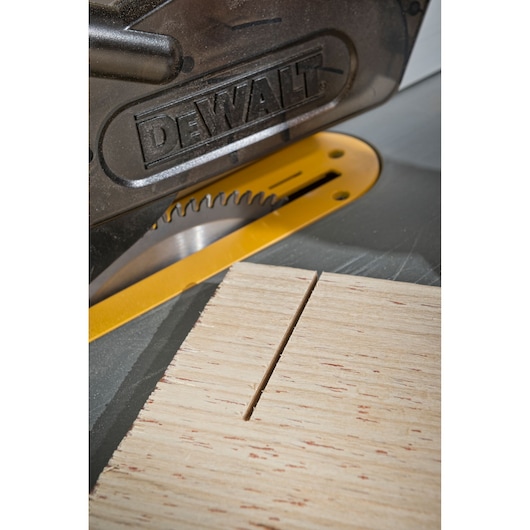 Close-up image of a DEWALT table saw cutting a piece of light-colored wood, showing the saw blade and a straight cut on the wooden surface.