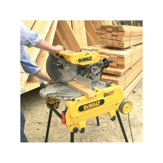 DEWALT miter saw cutting a wooden plank at a construction site with stacks of lumber in the background.