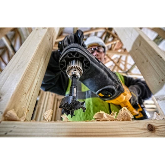 DEWALT drill with DT4585 bit creating a hole in wood during construction. Close-up on tool and wood chips.