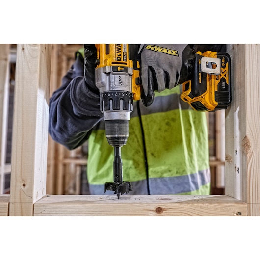 DEWALT cordless drill used to bore a hole in wooden beams in a construction setting, worker wearing gloves.