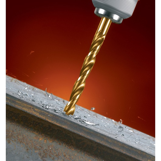 A close-up of a golden drill bit attached to a drill, drilling into a metal surface with metal shavings scattered around.
