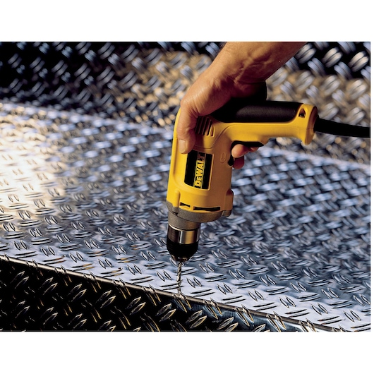 A DEWALT drill being used to drill into a metal plate with a textured surface.