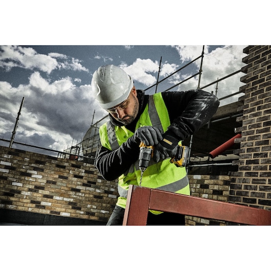 Worker in safety gear uses a DEWALT drill outdoors on a metal frame at a construction site.