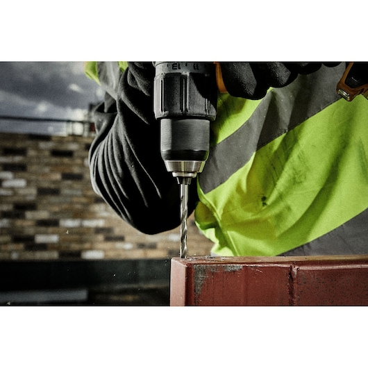 Close-up of gloved hand using a DEWALT drill to drill into metal, person in high-visibility jacket.