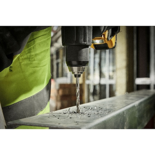 Close-up of a drill making a hole in a metal surface, with metal shavings around the bit.