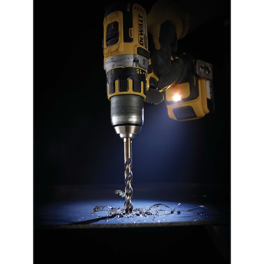 Cordless DEWALT drill with DT5557 bit drilling metal, with shavings and illuminated work area.