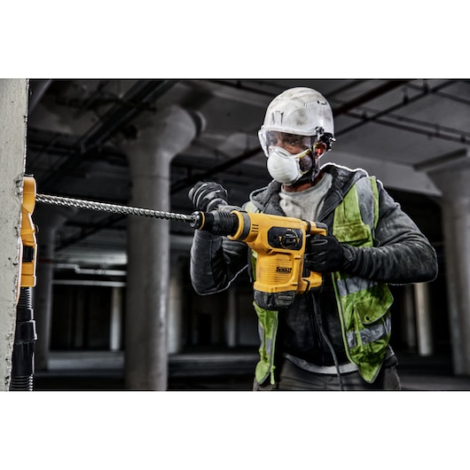 Worker uses DEWALT drill DT60820, DT60820-QZ on concrete; construction indoors, safety gear worn.