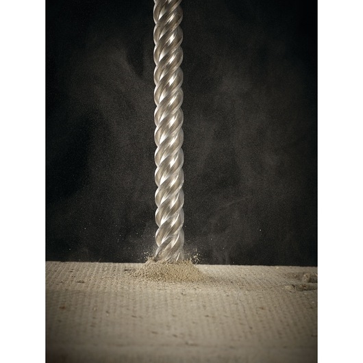 Close-up of a spiral drill bit making a hole in concrete, with dust visible around the tip.