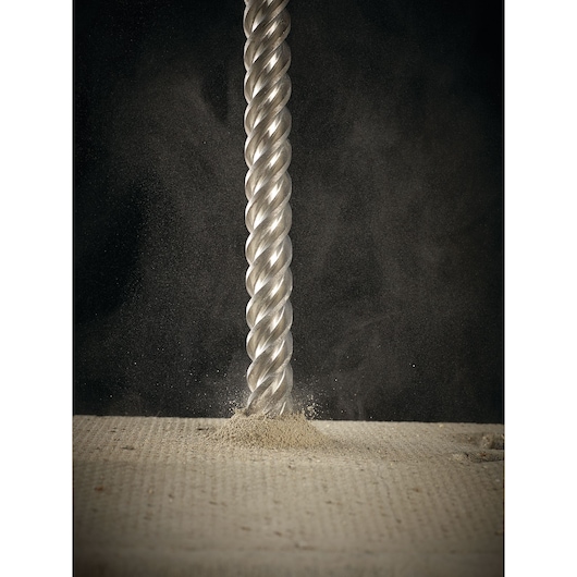 Close-up of a DEWALT drill bit penetrating a concrete surface, producing dust and debris.