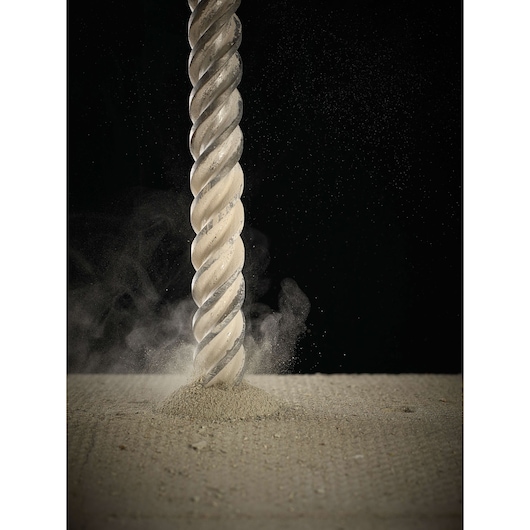 Close-up of a twisted masonry drill bit penetrating a concrete surface, creating dust and debris.