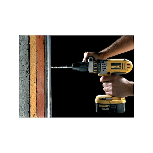 DEWALT drill in use, drilling into a concrete wall. Hands hold the yellow power tool against the surface.