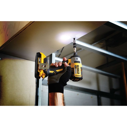 Person using a DEWALT cordless drill to drive a screw into a ceiling panel in an indoor construction setting.