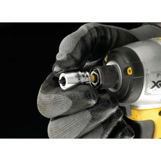 Gloved hand attaching DEWALT socket adaptor to a power tool with yellow and black handle.