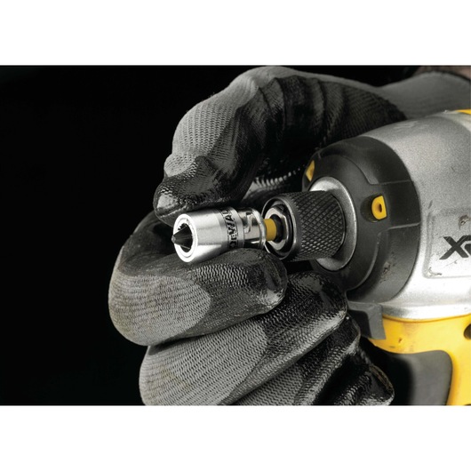 A close-up of a person wearing work gloves fitting a DEWALT socket onto a power tool against a black background.