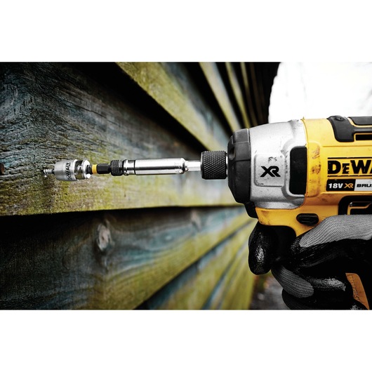 DEWALT drill with bit attached, in use on wooden siding outdoors, held by a gloved hand.