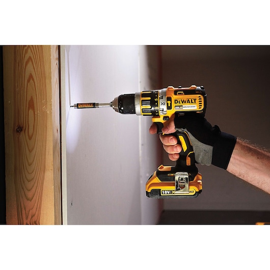 A hand using a DEWALT cordless drill to drive a screw into a wall next to a wooden beam.
