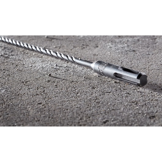 A close-up of a DEWALT SDS-plus drill bit lying on a textured concrete surface.