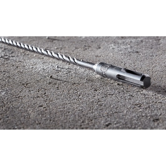 A close-up view of a DEWALT DT8922 SDS drill bit lying on a rough concrete surface.