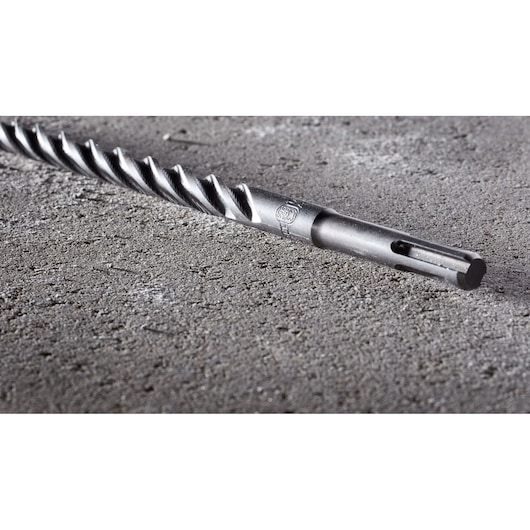 Close-up view of a DEWALT DT8931 SDS drill bit lying on a rough concrete surface, showing the spiral design and fitting end.