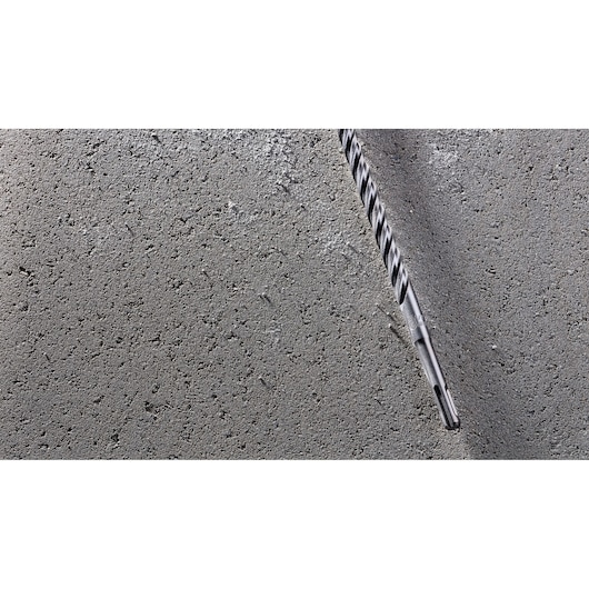 A DEWALT DT8938 masonry drill bit inserted into a concrete surface, showing the spiral fluting and SDS-plus shank.