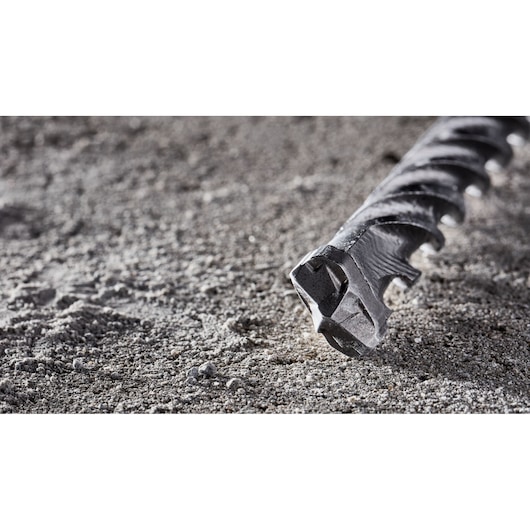 Close-up of the tip of a DEWALT drill bit resting on a rough, sandy surface.