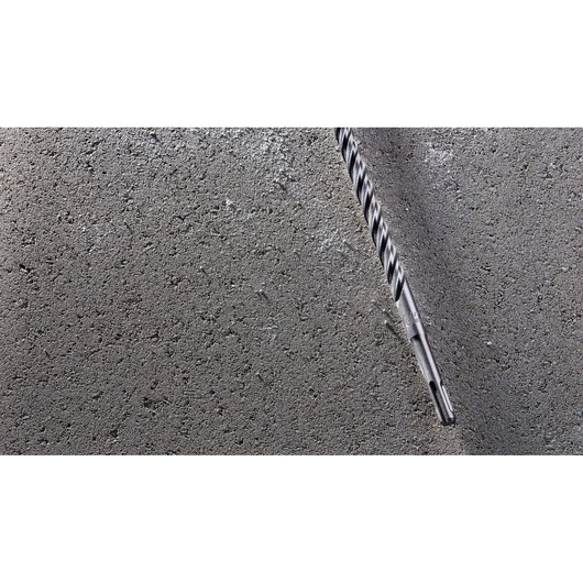 A close-up of a DEWALT masonry drill bit partially inserted into a rough concrete surface.