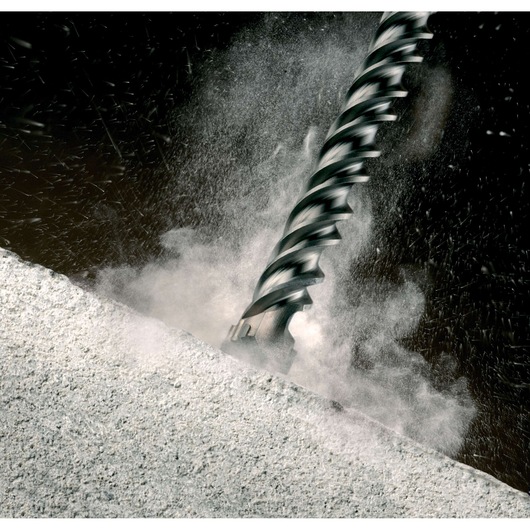 Close-up of a DEWALT drill bit cutting into concrete, with dust and debris flying.