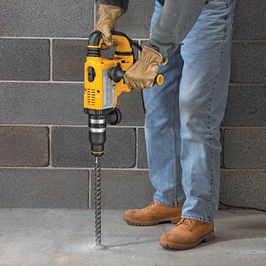 Person using a yellow DEWALT rotary hammer drill to drill into concrete floor.