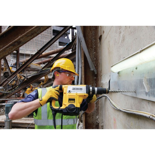 Person using a DEWALT hammer drill to drill into a concrete wall at a construction site.