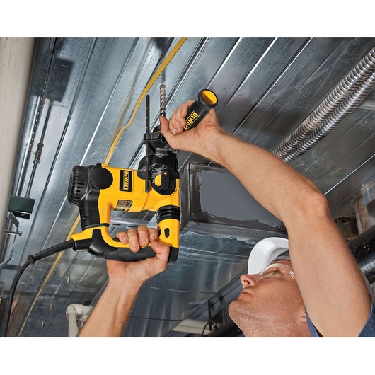 Person using a DEWALT drill to make a hole in a metal ceiling. The drill has a yellow and black design.